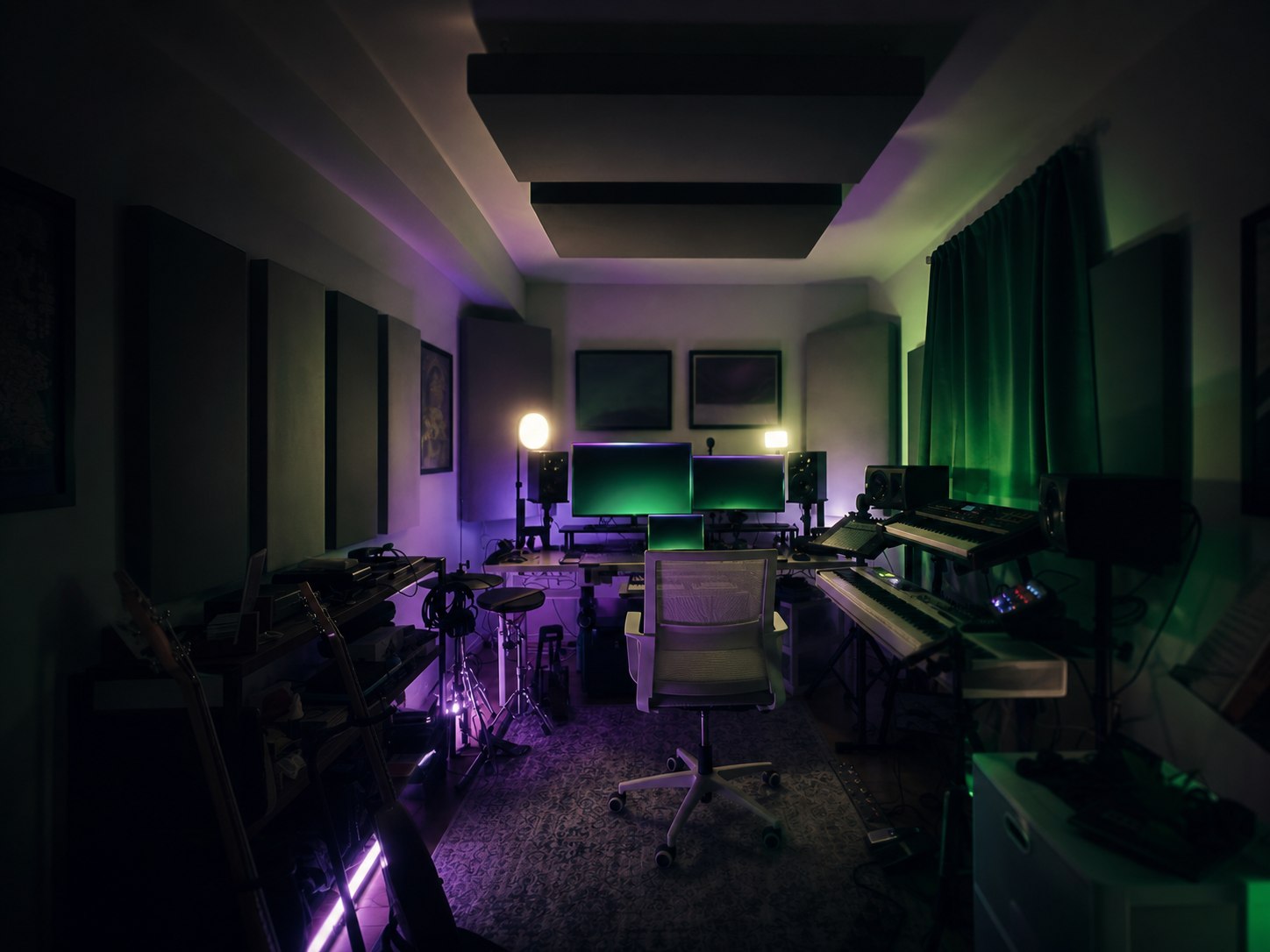 A dark, atmospheric home music studio with keyboards, speakers, acoustic treatment, and green and purple lighting